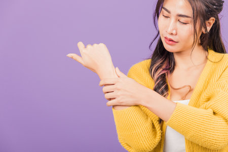 Portrait of Asian beautiful young woman sad with wrist pain from carpal tunnel syndrome, female hand injury feeling pain, studio shot isolated on purple background, Health care and medical conceptの写真素材