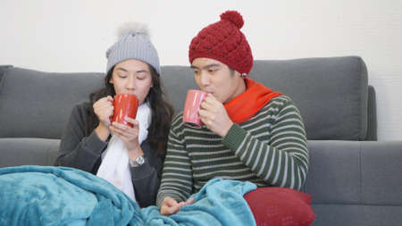 Happy Asian beautiful young family couple husband and wife smile relaxing. drinking tea, hot chocolate, coffee at christmas market in evening in home living room, winter holidays conceptの写真素材