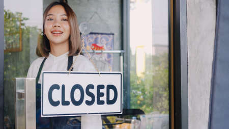 Happy Asian beautiful young woman staff turning round sign to close on door, Female owner of coffee shop closed the service on window, small businessの写真素材