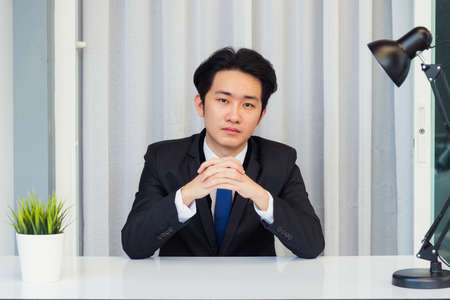 Work from home, Close up face of Asian young businessman video conference call  he looking to camera sitting and holding hands to listen to colleagues explain the work on desk at officeの写真素材
