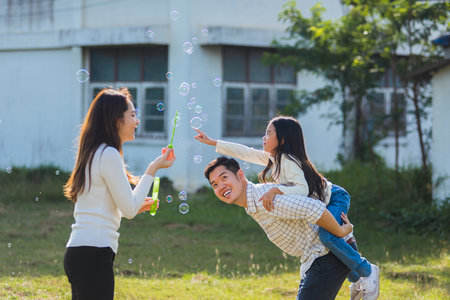 Happy Asian lifestyle family mother, father and little cute girl child having fun together and enjoying outdoor play blowing soap bubbles in the garden park on a sunny day, summertimeの写真素材