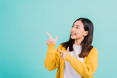 Portrait Asian beautiful young happy woman teen smiling show white teeth she's pointing finger up to side empty space studio shot isolated on blue background, Dental health conceptの写真素材