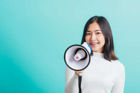 Beautiful Asian woman smile she holding megaphone making the announcement, female excited cheerful announce good news isolated on a blue backgroundの写真素材