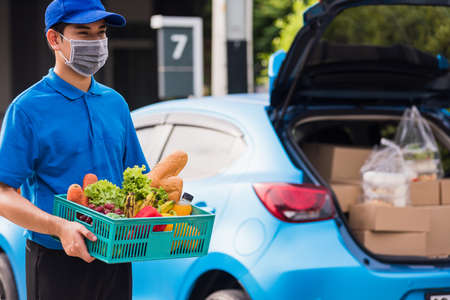 Asian grocery store delivery man wearing blue uniform and face mask protect he delivering fresh food...