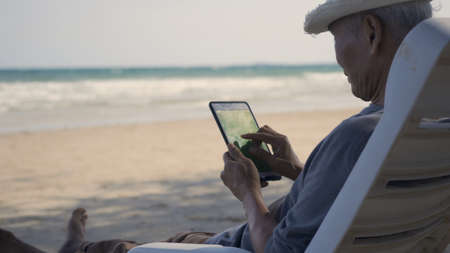 Senior man sitting on chairs enjoying time on beach travel vacation using tablet computer, Romantic elderly enjoy Travel summer vacation, plan life insurance at retirement conceptの写真素材