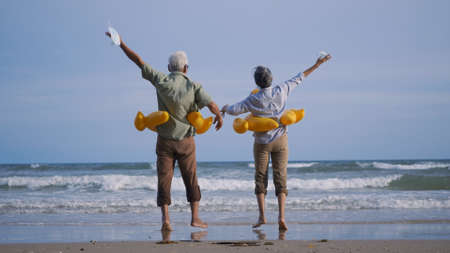 Happy senior couple wear rubber ring take off medical face mask and running to the beach enjoying life, relaxing after win coronavirus pandemic (COVID-19), plan life insurance at retirement coupleの写真素材