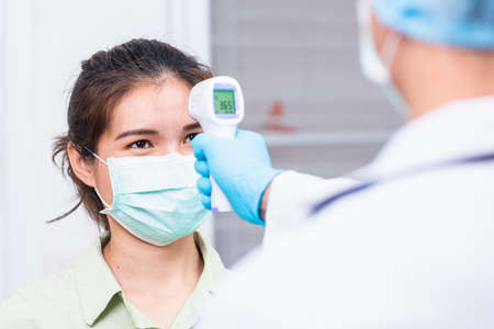 Doctor man use infrared forehead thermometer gun checking measuring patient body temperatureの写真素材