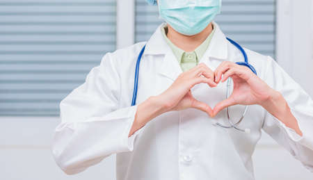 Closeup of doctor woman wearing white coat standing making heart finger shape, Doctor's hand sign, Healthy medical heart conceptの写真素材