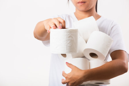 Closeup Asian young woman stocking up toilet paper for home panic in stores quarantine from virus. Female holding many rolls of toilet paper in arms on chest, studio isolated on white backgroundの写真素材