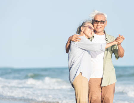 Happy Asian senior man and woman couple smile dancing resting relax on the beach honeymoon family sunny day, Romantic elderly enjoy travel summer vacation, plan life insurance at retirement coupleの写真素材