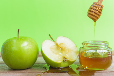 Jewish holiday, Apple Rosh Hashanah, the photo have honey in jar and drop honey on green apples on wooden with green backgroundの写真素材