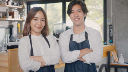 Portrait of happy handsome young man and beautiful woman confident cafe owner standing crossed arms on front counter bar together at the cafe coffee shop, Owner small business conceptの写真素材