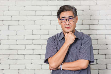 Portrait of Asian handsome senior elderly man wear eyeglasses on white brick wall background. Old man standing golden age grandfather healthcare cheerful lifestyleの写真素材