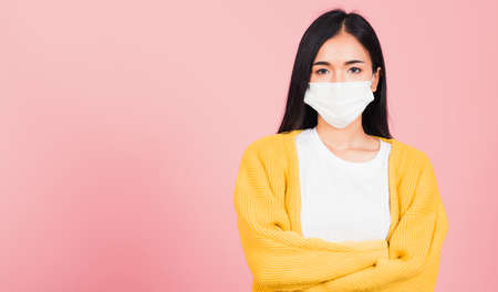 Asian beautiful young woman wearing medical mask protection for prevent infection virus, she crossed arms, studio shot isolated on pink background copy space medical health care conceptの写真素材