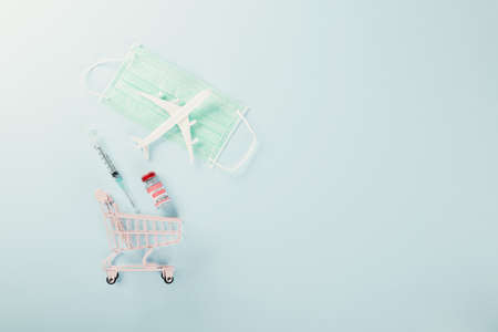 Shopping cart with vaccine vials bottles for vaccination, model plane and medicine face mask vaccine transportation concept, buy vaccine, studio shot isolated blue background with copy space for textの写真素材