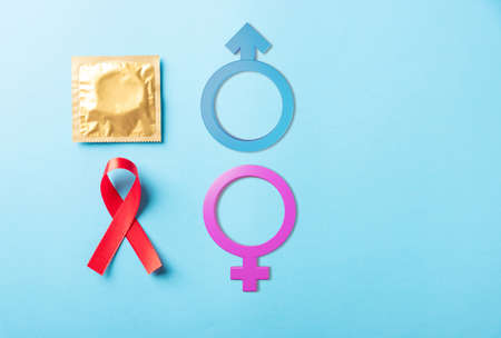 Red bow ribbon symbol HIV, AIDS cancer awareness, condom with shadows and Male, female gender signs, studio shot isolated on blue background, Healthcare medicine sexually concept, World AIDS Dayの写真素材
