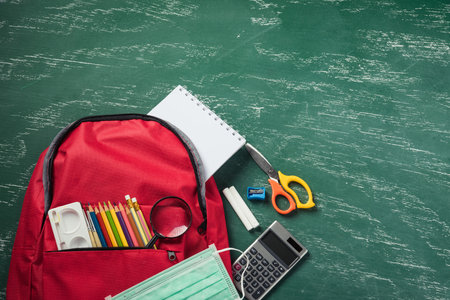 Top view of stylish red school bag backpack at a green blackboard with face mask protection and stationery, Back to school education new normal during outbreak COVID-19 or coronavirus conceptの写真素材