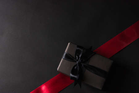 Black Friday Sale concept, Top view of gift box wrapped black paper and black bow ribbon press, studio shot on and having red ribbon across a dark backgroundの写真素材