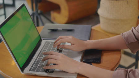 Businesswoman sitting alone working typing keyboard on laptop computer green screen at cafe coffee...