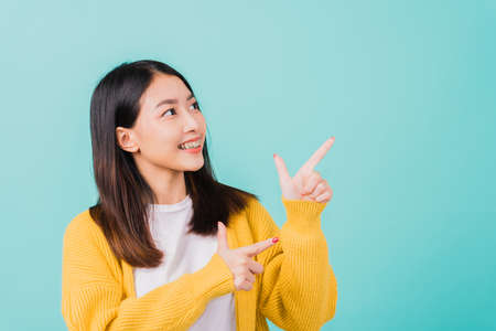 Portrait Asian beautiful young happy woman teen smiling show white teeth she's pointing finger up to side empty space studio shot isolated on blue background, Dental health conceptの写真素材