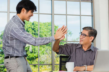 Asian senior and young business man greeting each other in the office. Happy old and junior two businessmen greet touch hand, greeting and partnership conceptの写真素材