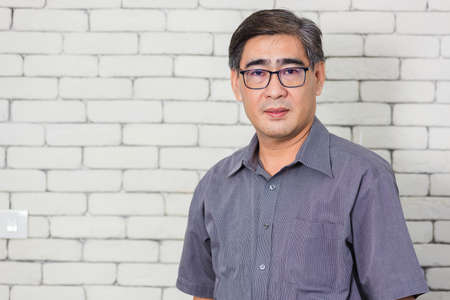 Portrait of Asian handsome senior elderly man wear eyeglasses on white brick wall background. Old man standing golden age grandfather healthcare cheerful lifestyleの写真素材