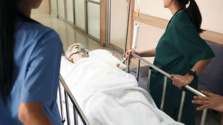 Emergency Department. Nurse and senior doctor team busy push emergency stretcher transport senior patient in hospital, doctors, nurses in surgical gown and white coat uniform running with hurryの写真素材