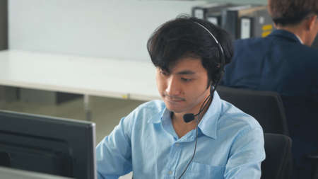 Call center young employee working with headset, Smiling customer support operator team at work surrounded by colleagues working in the office, Helpdesk customer services support agent conceptの写真素材