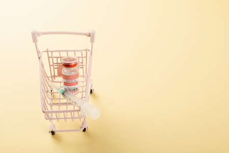 Shopping cart with vaccine vials bottles and syringes for vaccination against coronavirus, medicine illness, COVID-19 disease vaccine studio shot isolated on yellow backgroundの写真素材