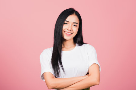 Asian happy portrait beautiful cute young woman standing her smile confidence with crossed arms isolated, studio shot on pink background and copy space, Thai female looking to cameraの写真素材