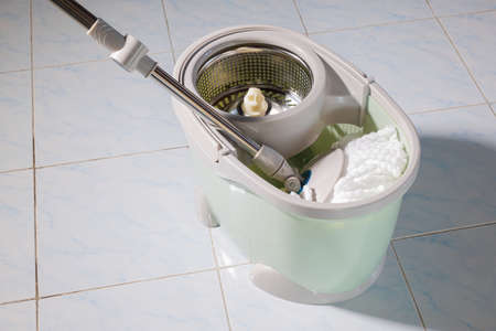 Mop with microfiber head spinning on the bucket next to floor cleaning liquid and mopping the floor...