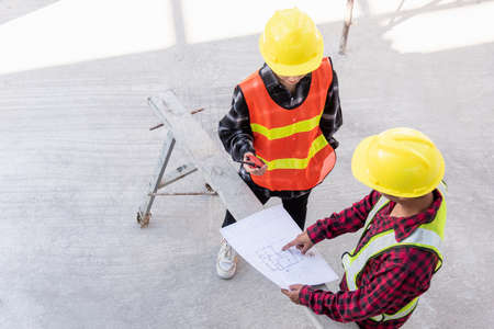 Architect and client discussing help create plan with blueprint of the building at construction site floor. Asian engineer foreman worker man and woman meeting and planning construction work, top viewの写真素材
