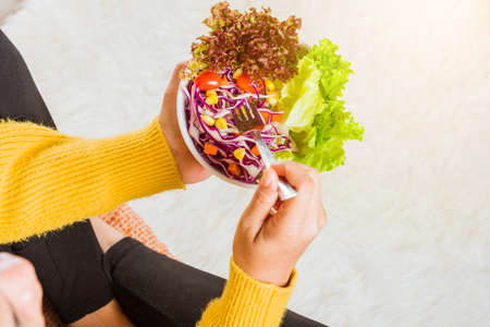 Top view of female hands holding bowl with green lettuce salad on legs, a young woman eating fresh salad meal vegetarian spinach in a bowl, Clean detox healthy food conceptの写真素材