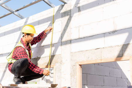 Construction worker or contractor man using measuring tape checking from steel  roof frame to the door on building construction site, foreman taking measurements wall while workingの写真素材