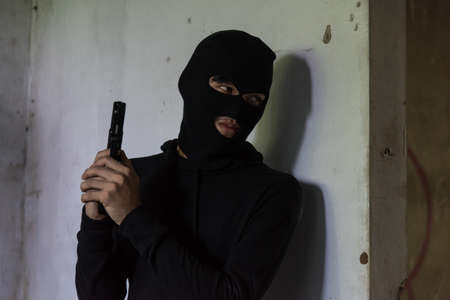 Man robber thief wear mask holding gun hiding armed waiting criminalの写真素材