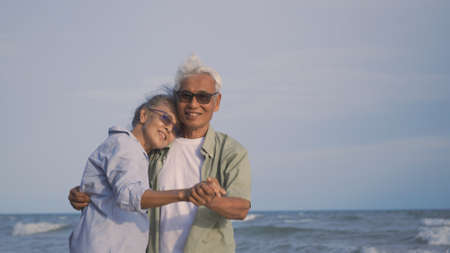 Happy Asian senior man and woman couple smile dancing resting relax on the beach honeymoon family sunny day, Romantic elderly enjoy travel summer vacation, plan life insurance at retirement coupleの写真素材