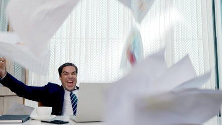 Happy business man excited surprised work at white office desk with pc laptop throwing up paper...