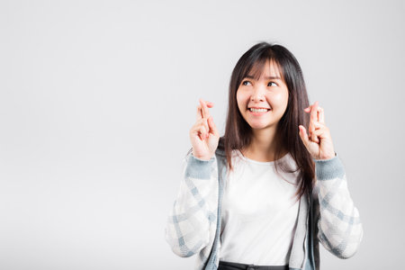 Happy woman have superstition her holding fingers crossed for good luck gesture, Asian beautiful young female smiling superstition, studio shot isolated on white background with copy spaceの写真素材