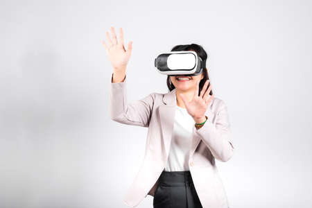Smiling woman confidence excited wear VR headset device touching air during virtual reality experience isolated white background, Asian happy portrait female playing video game studio shot, copy spaceの写真素材