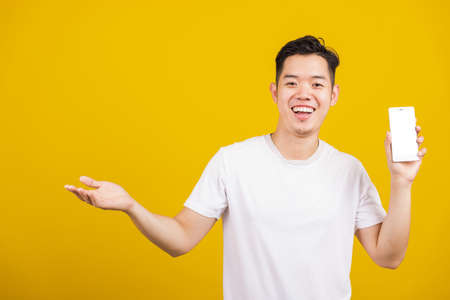 Asian handsome young man smiling positive showing mobile phone blank screen with another hand palm...