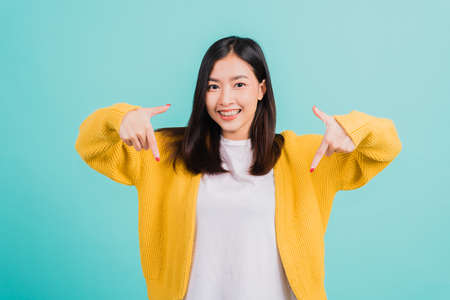 Portrait Asian beautiful young happy woman teen smiling show white teeth she's pointing finger down to empty space studio shot isolated on blue background, Dental health conceptの写真素材