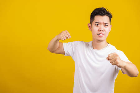 Asian handsome young angry man showing punch a clenches fist, aggressive male punching towards the camera looking to camera, studio shot isolated on yellow backgroundの写真素材
