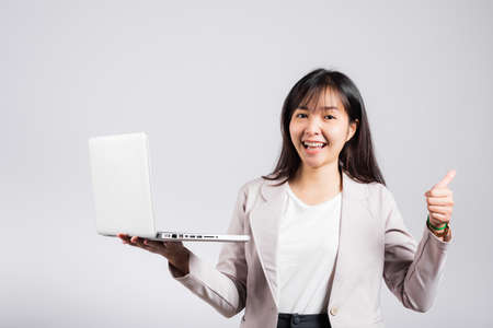 Woman smile confident smiling face hold using laptop computer and showing thumb up for like gesture, Portrait excited Asian young female person businesswoman studio shot isolated on white backgroundの写真素材