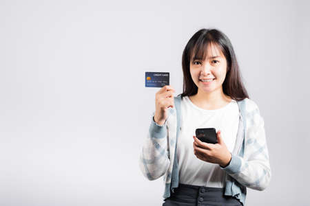 Woman excited smiling hold mobile phone and plastic debit credit bank card for payment studio shot isolated white background, happy young female using smartphone buy and pay online shoppingの写真素材