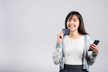 Woman excited smiling hold mobile phone and plastic debit credit bank card for payment studio shot isolated white background, happy young female using smartphone buy and pay online shoppingの写真素材