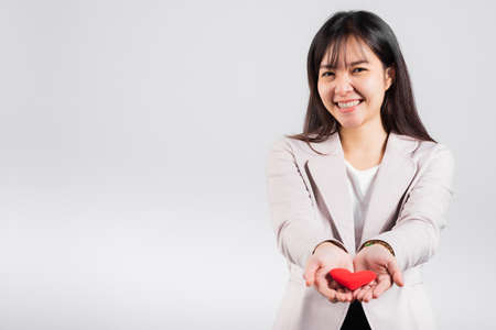 Smiling woman confidence showing holding red heart with her hand palm isolated white background, Asian happy portrait beautiful young female send love and happy valentine in studio shot, copy spaceの写真素材