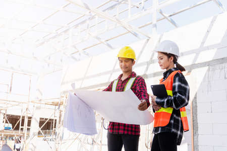 Architect and client discussing the plan with blueprint of the building at construction site. Asian...
