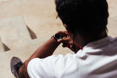 Close up Asian young athlete sport runner black man wear modern time smart watch he sitting resting before training running at the outdoor street health park, healthy exercise before workout conceptの写真素材