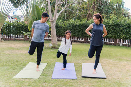 Asian young mother, father and child daughter practicing exercising stretching together before yoga workout outdoor morning in nature a field garden park. Happy family kid sport healthy lifestyleの写真素材