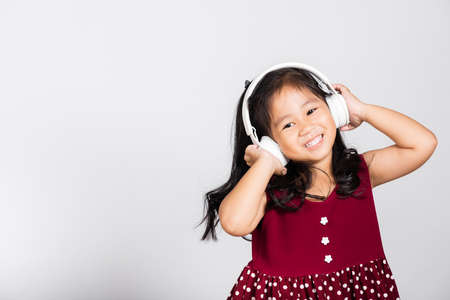 Little cute kid girl 3-4 years old listen music in wireless headphones in studio shot isolated on white background, happy Asian children smiling listening audio, entertainment lifestyleの写真素材